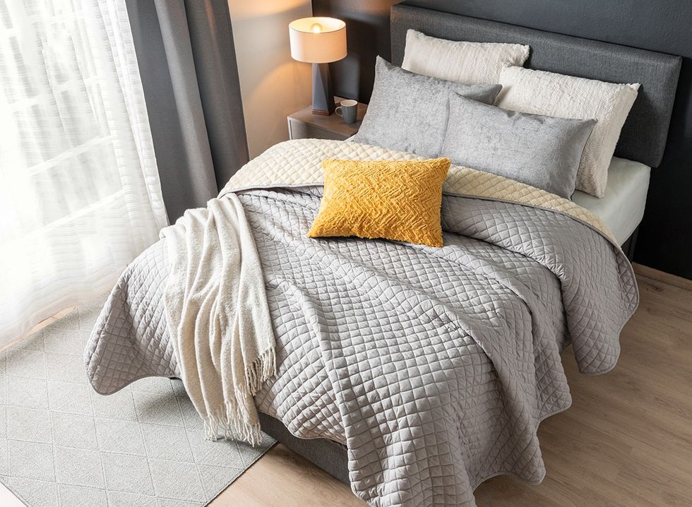 A bedroom with textured blankets, pillows, upholstered headboard, rug and curtains