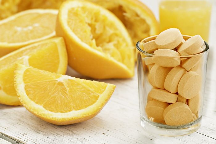 A close up shot of sliced and squeezed oranges a glass of orange juice and a glass full of orange flavored vitamin C Pills