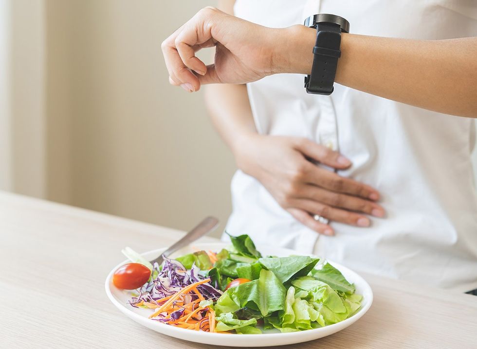 A plate of salad on a table and a hungry person looking at their watch