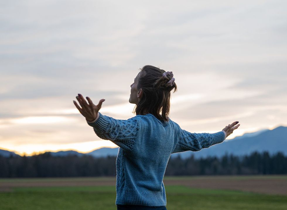 A smiling woman standing in a field with her arms out