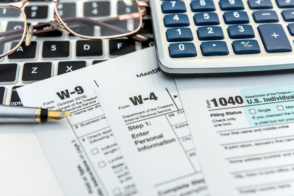 A stack of tax forms on top of a keyboard next to a pair of glasses and a calculator