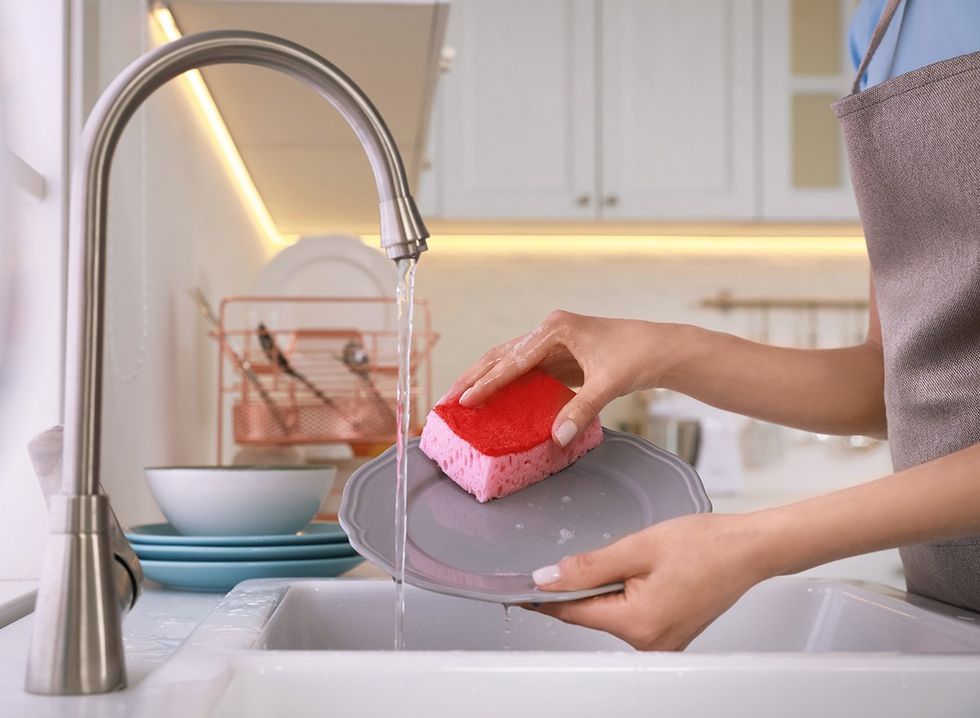 A woman in the kitchen washing dishes using a sponge 