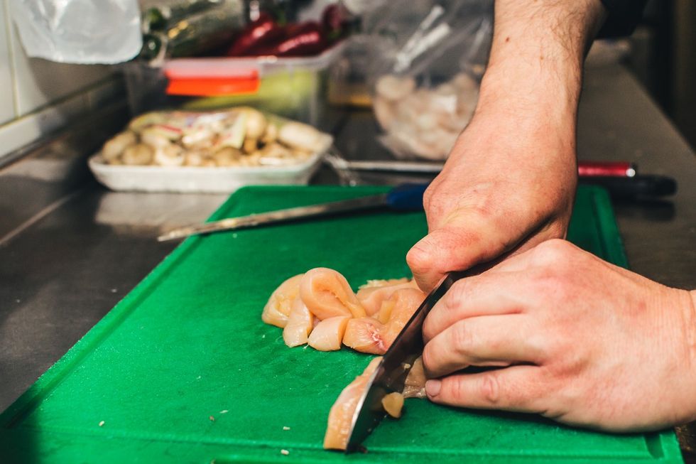 Close up of a person cutting chicken on a plastic cutting board.