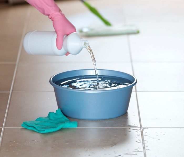 gloved hand pouring bleach into bucket