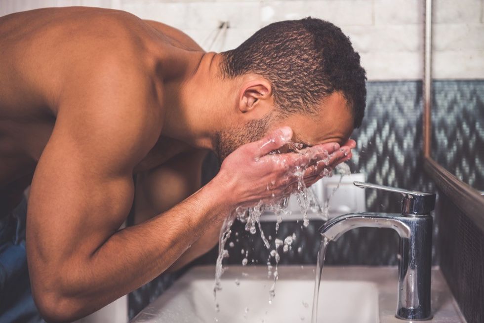 man washing his face at a sink in the bathroom