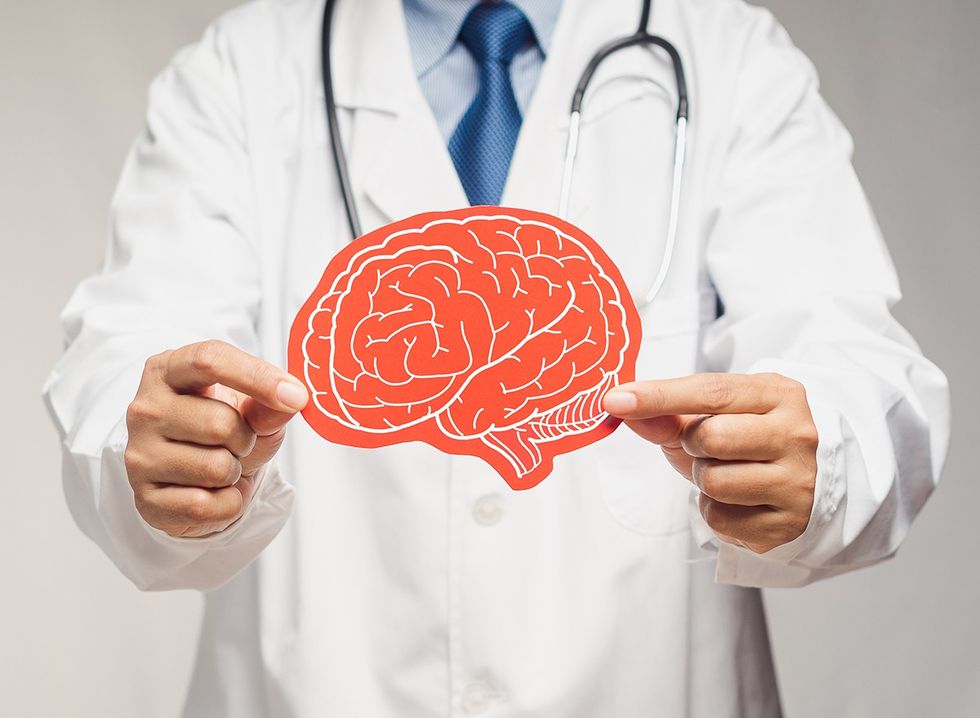 Midsection of a doctor in a uniform holding a brain symbol made from red paper 