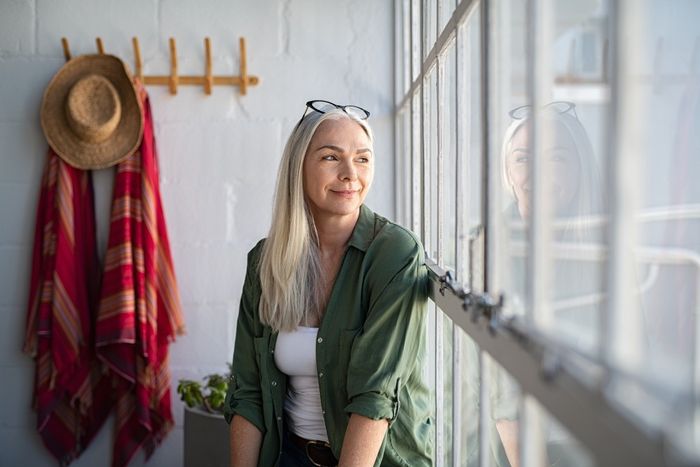 smiling mature woman looking outside window. Thoughtful old woman looking away through window. Senior beautiful woman sitting at home with pensive expression.