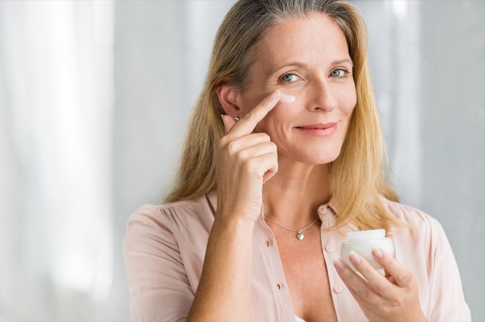 Smiling senior woman applying anti-aging lotion to remove dark circles under eyes.