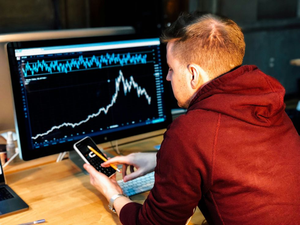 someone looks at investments on their phone and computer screen