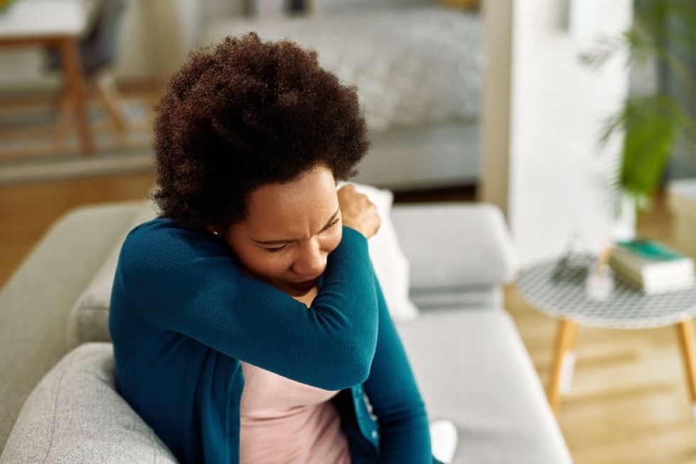 woman coughing into her arm while sitting on the couch