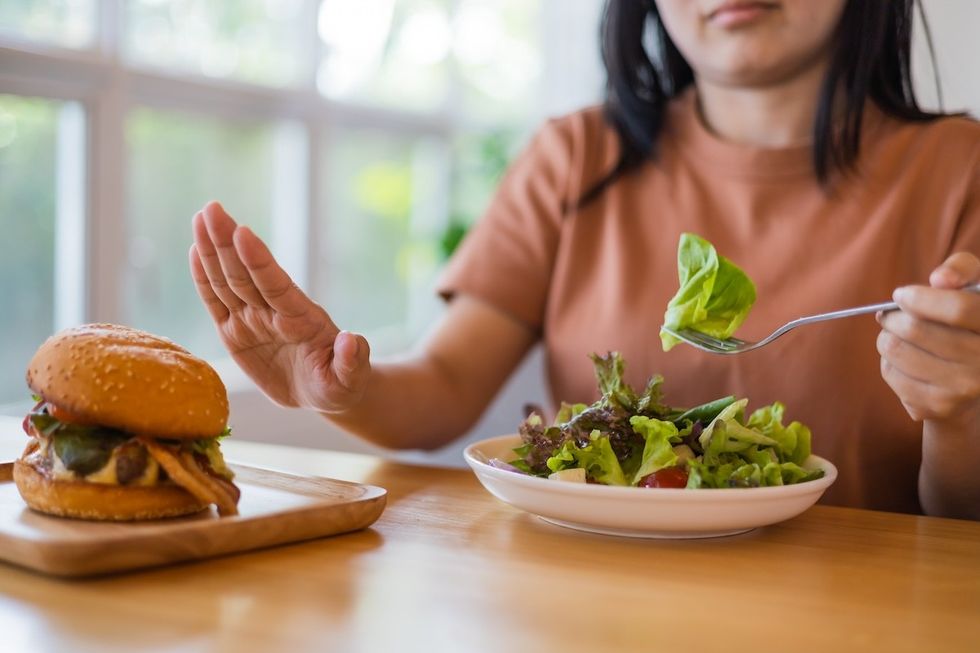 Woman eating a salad at the table, pushing away a hamburger