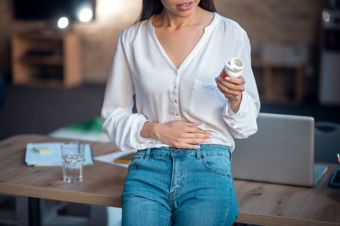 Woman holding her stomach in pain, looking at a bottle of medication