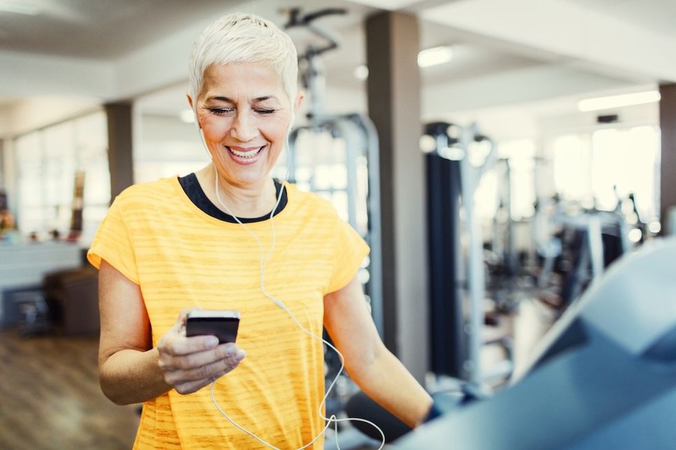 woman in a yellow t-shirt looking at her phone while on the treadmill