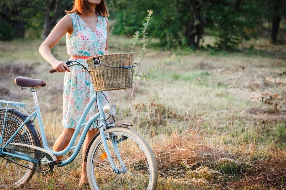 woman in spring dress with a blue bicycle in a field of grass