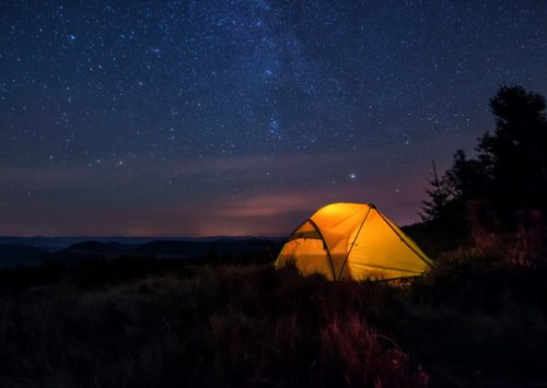iluminated tent under stars in the mountains