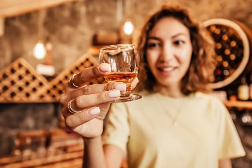Happy asian woman tastes a new brand of cognac from a glass at the winery. The concept of strong alcohol and brandy