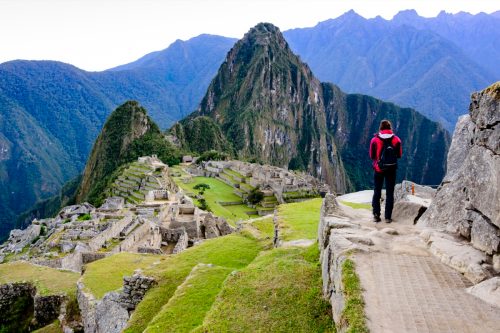 Woman standing on a ledge and overlooking the Inca ruins of the city of Machu Picchu seen in the background.