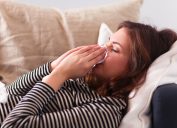 woman sneezing on couch, contagious conditions