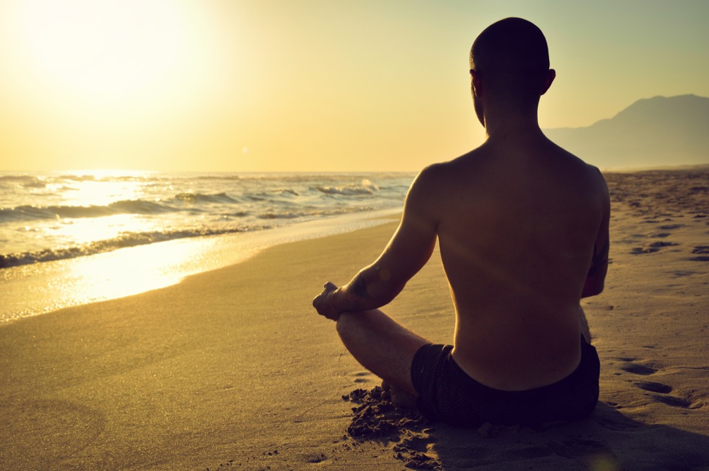 man sits on sandy beach as gun glares while meditating