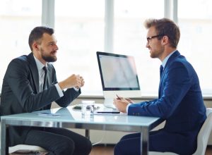 A businessman conducting an interview at his desk with a computer.