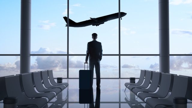 man stands in an airport gate watching a plane take off