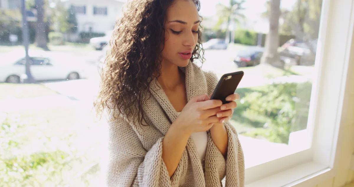woman on her phone in windowsill, The best opening lines for online dating