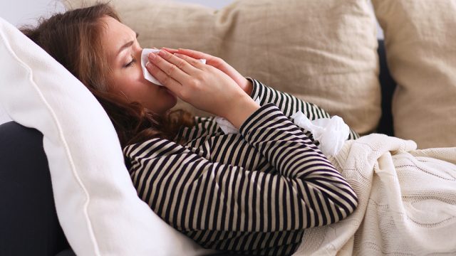 woman sneezing sick on the couch