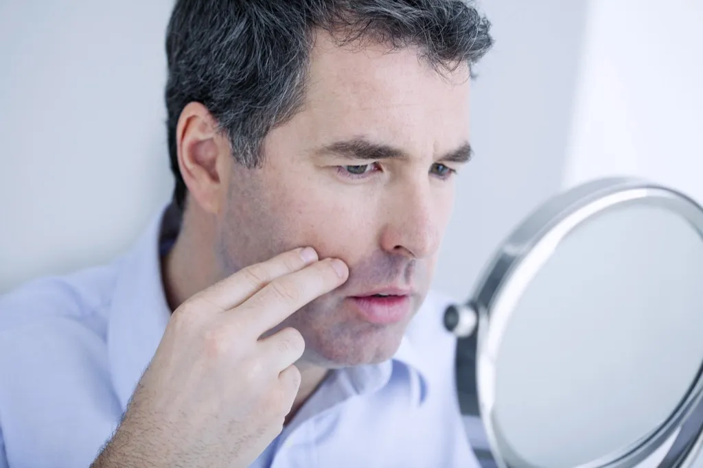 man looking at skin in mirror body changes over 40