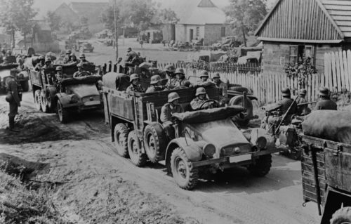 Black and white photo of troops riding in trucks during WWII