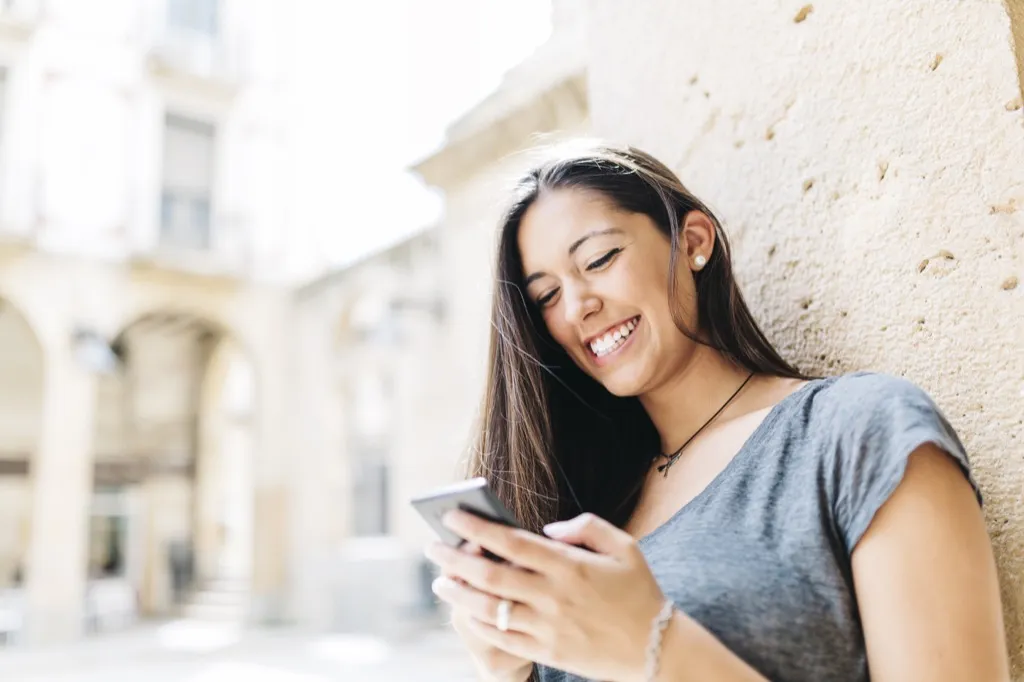 woman looking at her phone and smiling, The best opening lines for online dating