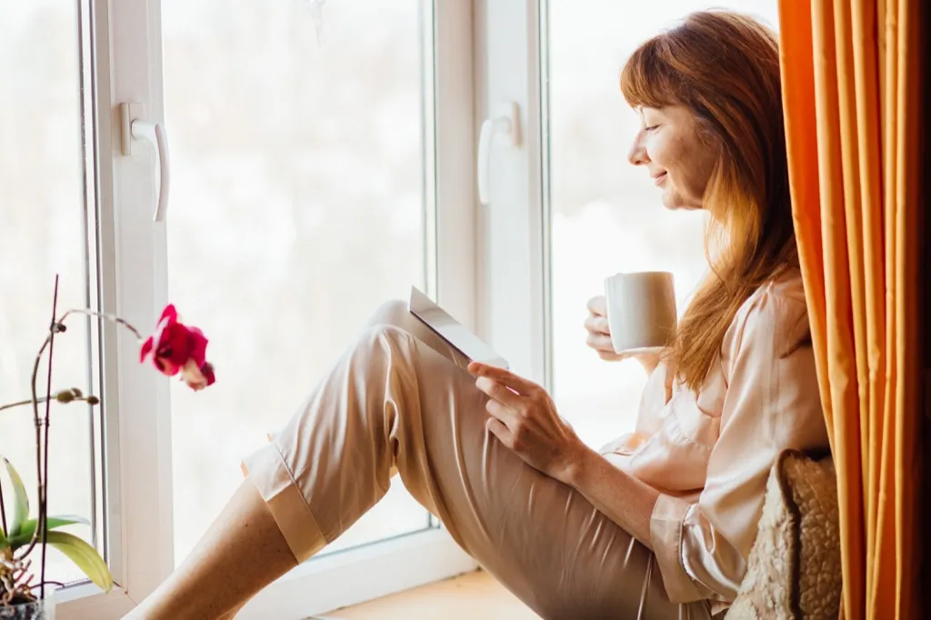 woman looking out window with a coffee - being single 
