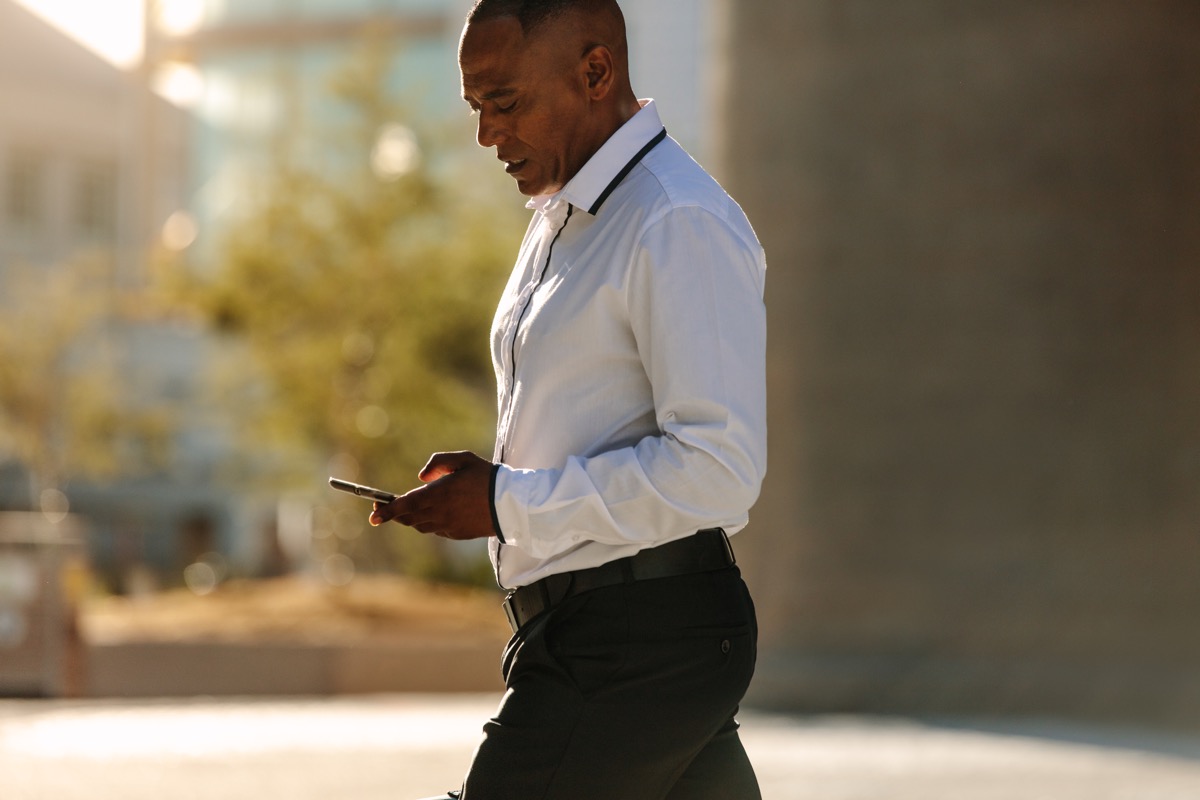 Black Man Looking at his Phone while he Walks to Work Healthy Man