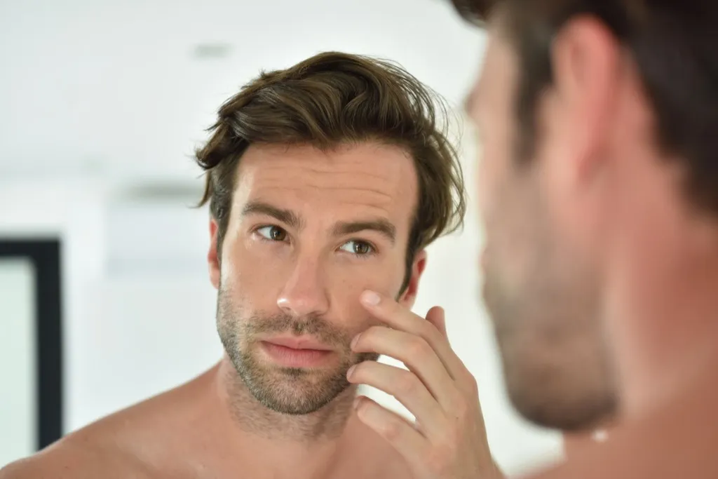 man looking in the mirror for wrinkles - look younger