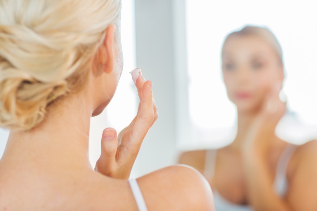 woman applying retinol in the mirror look younger