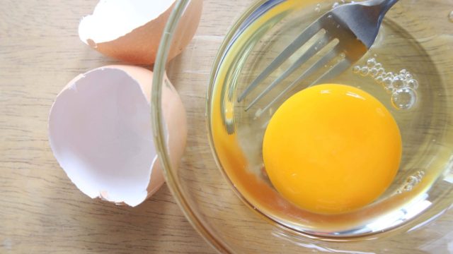 Raw egg in a clear bowl with shells and fork
