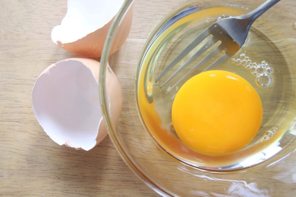 Raw egg in a clear bowl with shells and fork