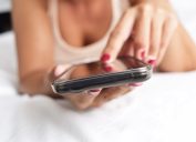 woman's hand types on smartphone in bed, early signs of alzheimer's
