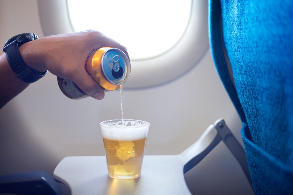 Un bărbat toarnă mai multă bere în ceașca lui în avion