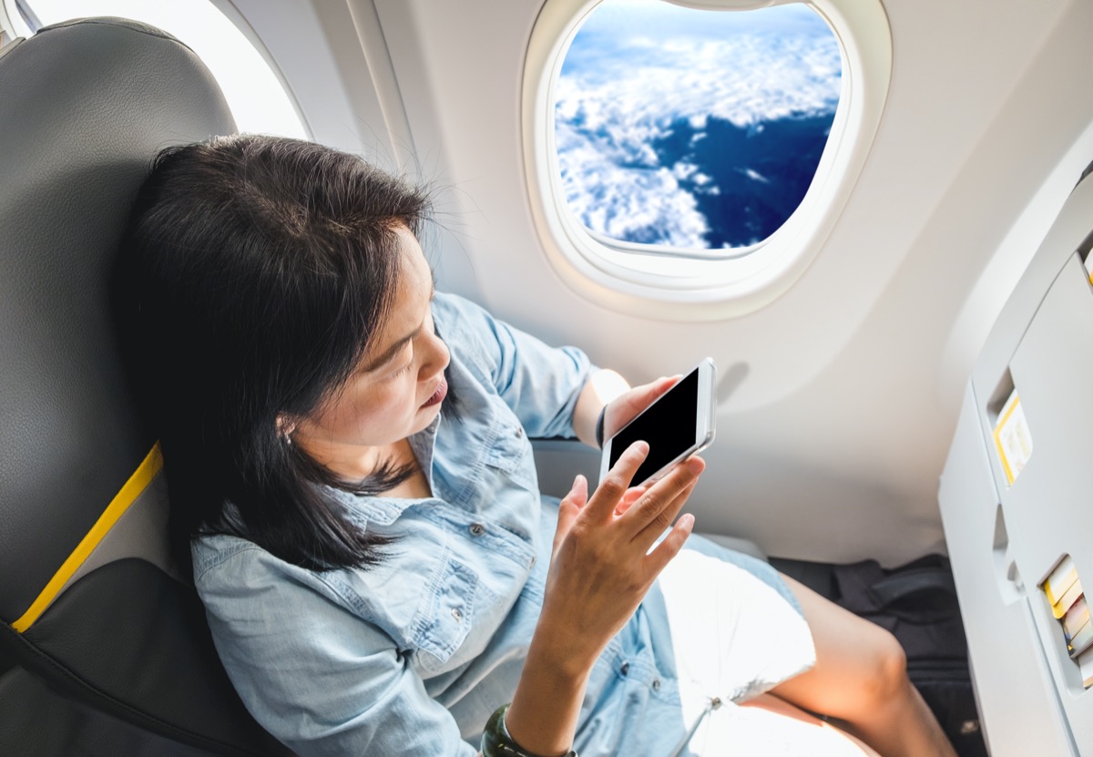 Asiatische Frau, die ihr Telefon im Flugzeug benutzt