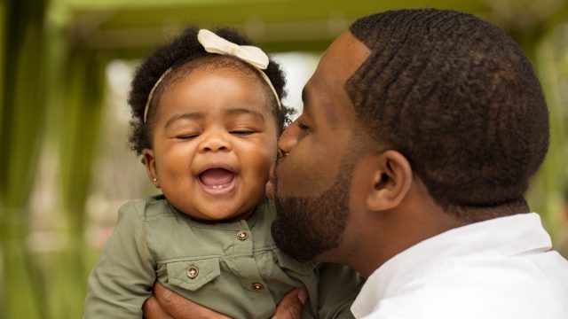 young black dad kissing baby daughter