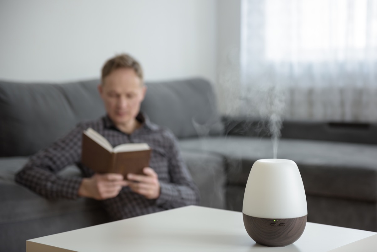 Aromo diffuser on a white table on the background of the interior. In the background, a man is reading a book.