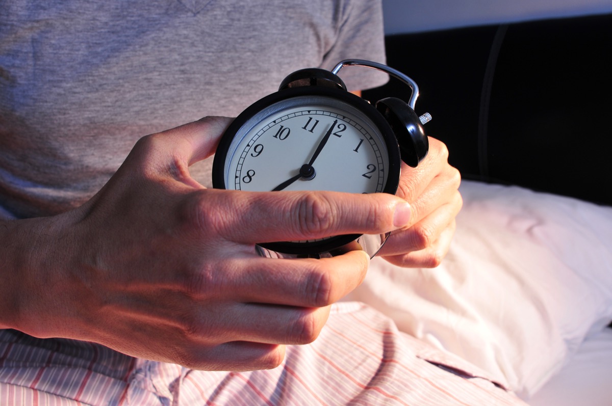 Person setting clock at bed time for alarm clock