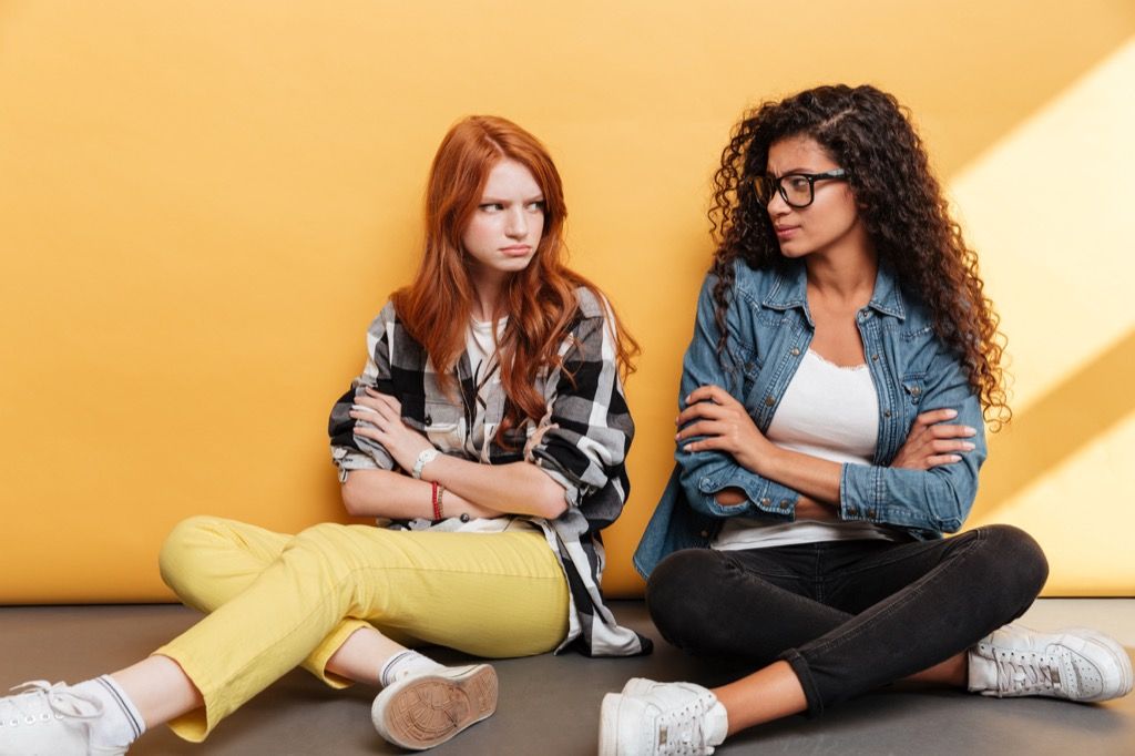 white woman with red hair and black woman with curly hair and glasses look at each other angrily