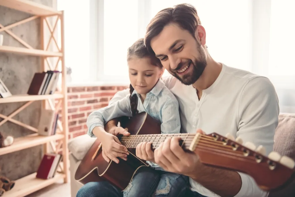 man holding young girl, teaching her to play guitar