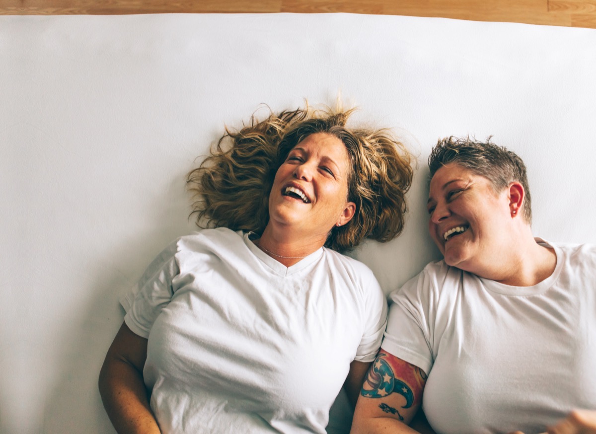 Lesbian couple joyfully laughing while laying in bed, habits after 40