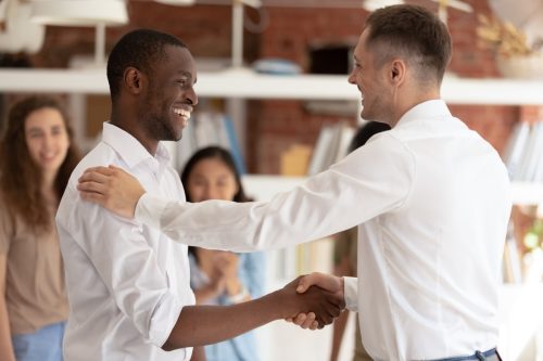 Boss thanking congratulating employee shaking hands multicultural