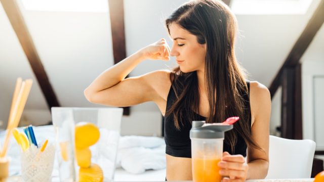 woman drinking juice and making a muscle with bicep