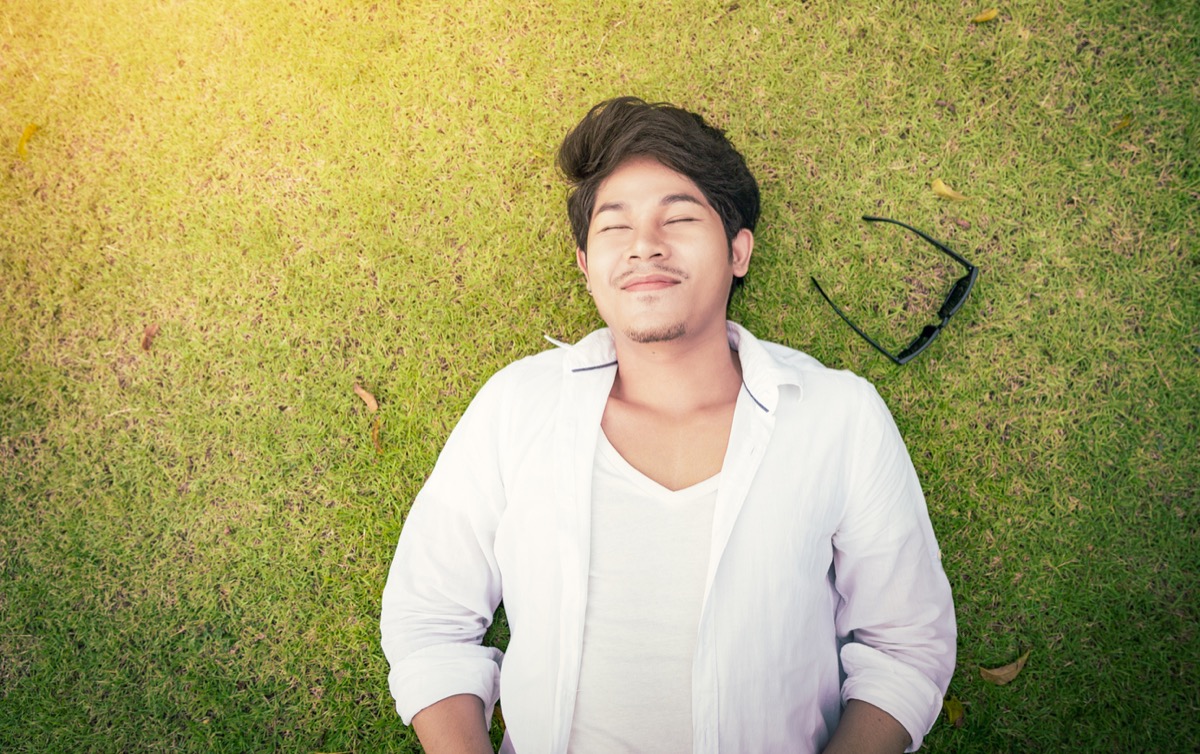 young asian man lying on the grass with his eyes closed and his sunglasses next to him