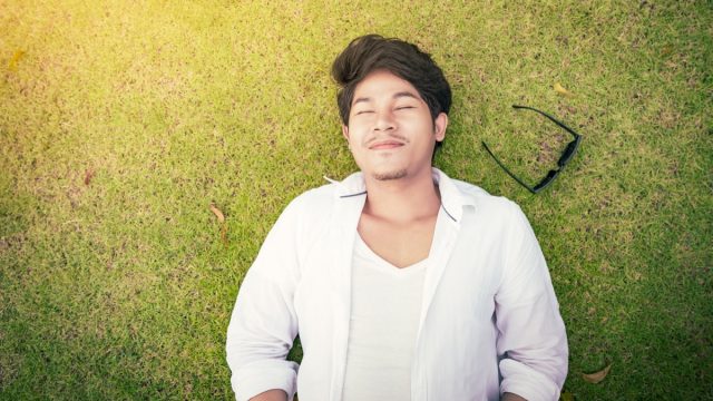 young asian man lying on the grass with his eyes closed and his sunglasses next to him