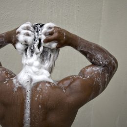 black man with his back to camera shampooing his hair in the shower
